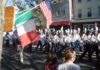 Parade Fundraiser: Comedy Night at the Harbor this Thursday Parade marchers in uniform with plumed hats marching down a street, carrying Italian and American flags as spectators watch from the curb.