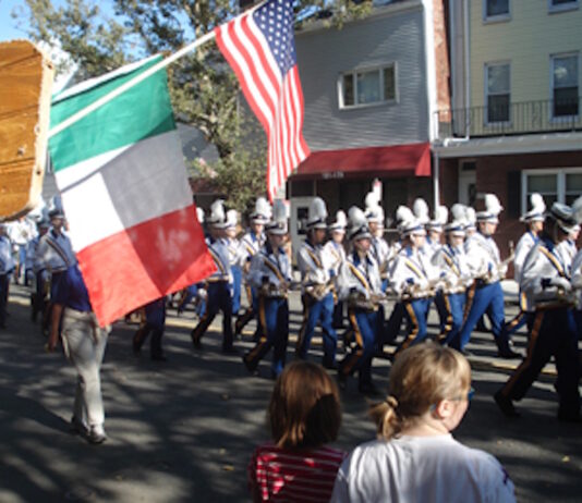Parade Fundraiser: Comedy Night at the Harbor this Thursday Parade marchers in uniform with plumed hats marching down a street, carrying Italian and American flags as spectators watch from the curb.