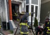 Social Centers establishes fund for victims of Princeton Street fire Firefighters in turnout gear handling large hoses on a residential street, preparing entry into a house with crews in the doorway.
