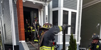 Social Centers establishes fund for victims of Princeton Street fire Firefighters in turnout gear handling large hoses on a residential street, preparing entry into a house with crews in the doorway.