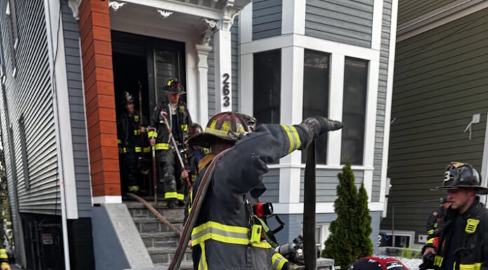 Social Centers establishes fund for victims of Princeton Street fire Firefighters in turnout gear handling large hoses on a residential street, preparing entry into a house with crews in the doorway.