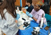 Photo gallery: What we saw at the East Boston High School’s STEAM event Saturday, May 9 Group of people in gloves conducting a hands-on science experiment at a table with microscopes and lab gear.
