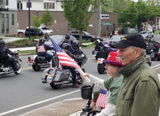 Set the date: 5/17 — 15th Annual Wounded Veterans Run Motorcycle parade on a city street; riders with American flags pass by while spectators on the curb wave flags.