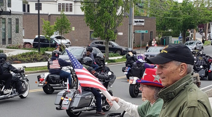 Set the date: 5/17 — 15th Annual Wounded Veterans Run Motorcycle parade on a city street; riders with American flags pass by while spectators on the curb wave flags.