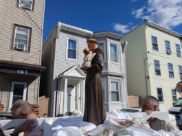 Sacred Heart marks the feast of St. Anthony with annual procession Statue of a saint holding the baby Jesus on a float, carried during a street parade, with row houses in the background.