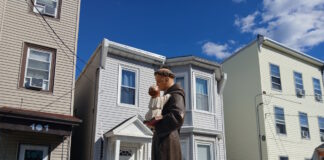 Sacred Heart marks the feast of St. Anthony with annual procession Statue of a saint holding the baby Jesus on a float, carried during a street parade, with row houses in the background.