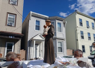 Sacred Heart marks the feast of St. Anthony with annual procession Statue of a saint holding the baby Jesus on a float, carried during a street parade, with row houses in the background.
