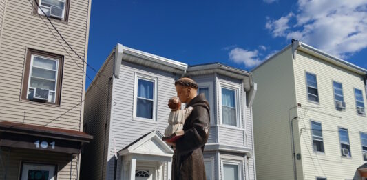 Sacred Heart marks the feast of St. Anthony with annual procession Statue of a saint holding the baby Jesus on a float, carried during a street parade, with row houses in the background.