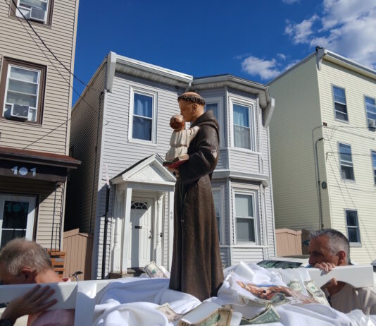 Sacred Heart marks the feast of St. Anthony with annual procession Statue of a saint holding the baby Jesus on a float, carried during a street parade, with row houses in the background.