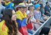 Scenes from the Columbia v. Portugal watch party at East Boston Stadium Spectators at a stadium, a woman with a striped hat and a Colombian flag draped over her shoulders, clapping.