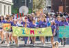 ZUMIX to host 2026 Walk for Music Diverse group marching in a street parade, holding a bright lime banner that reads ZUMIX and colorful signs around them.
