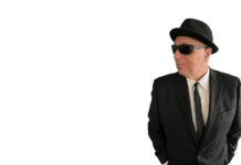 Sal Baglio’s new record is coming out in July Man in a black suit and tie wearing a hat and sunglasses, looking to the right with hands in pockets.