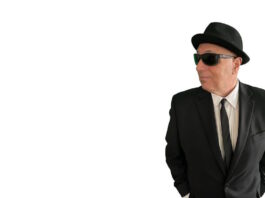 Sal Baglio’s new record is coming out in July Man in a black suit and tie wearing a hat and sunglasses, looking to the right with hands in pockets.