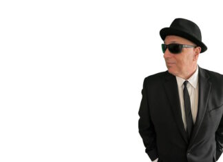 Sal Baglio’s new record is coming out in July Man in a black suit and tie wearing a hat and sunglasses, looking to the right with hands in pockets.