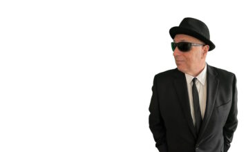 Sal Baglio’s new record is coming out in July Man in a black suit and tie wearing a hat and sunglasses, looking to the right with hands in pockets.