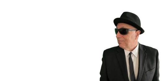 Sal Baglio’s new record is coming out in July Man in a black suit and tie wearing a hat and sunglasses, looking to the right with hands in pockets.