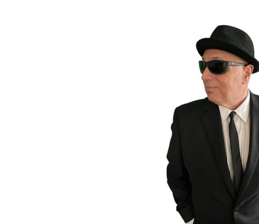 Sal Baglio’s new record is coming out in July Man in a black suit and tie wearing a hat and sunglasses, looking to the right with hands in pockets.