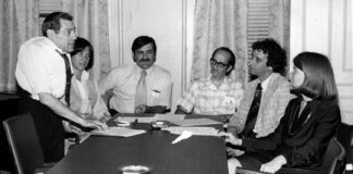 Gina Fiandaca: Appreciating John Vitagliano, who always believed in people Six professionals in a office meeting around a long conference table; a man stands presenting papers to seated colleagues.