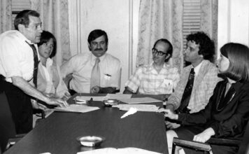 Gina Fiandaca: Appreciating John Vitagliano, who always believed in people Six professionals in a office meeting around a long conference table; a man stands presenting papers to seated colleagues.