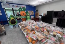 Maverick Landing Community Services launches Grab & Go produce market, expanding affordable fresh food access across East Boston Volunteers in avocado and carrot costumes pose behind tables stacked with grab-and-go produce bags at a community food drive.