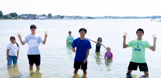 Two hundred fifty kids Boston kids had a blast at Save the Harborโs Annual Eastie Beach Bash Group of kids standing in knee-deep water at the beach, posing and making peace signs.