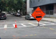 Residents and businesses are fed up with the parking situation in East Boston Orange 'Road Closed' sign with a black left arrow and a traffic cone on a city street near a crosswalk, indicating road construction.